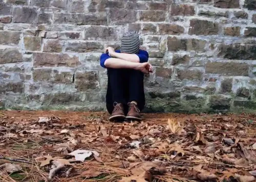A person who is suffering sitting alone near a wall.