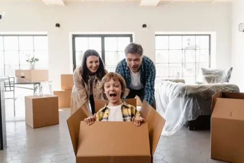 Family of three playing with cardboard boxes while unpacking after their move