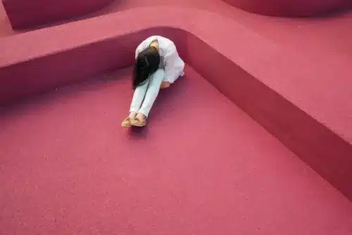 a woman dressed in white sitting on a red floor with her head hanging low