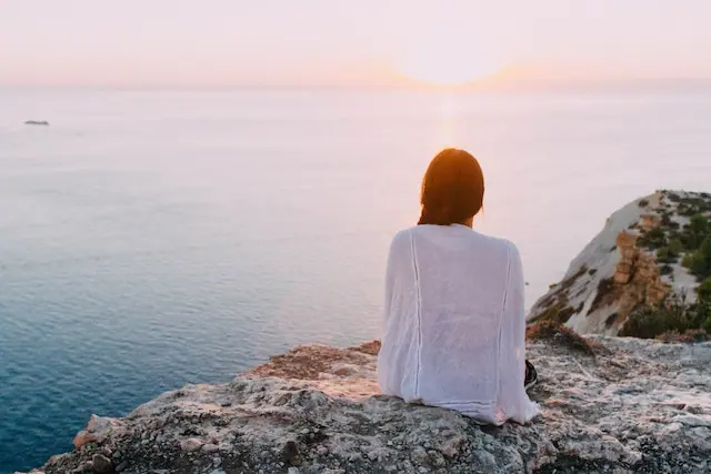 woman sitting on a cliff near the sea