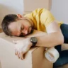 Man looking sad and depressed lying on top of a moving box to symbolize moving and mental health challenges