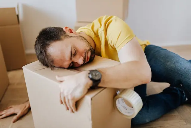 Man looking sad and depressed lying on top of a moving box to symbolize moving and mental health challenges