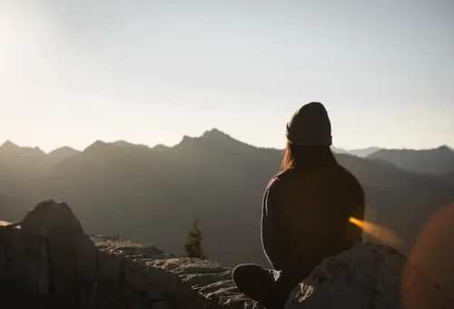 woman sitting on a rock and meditating while sungazing depicts the benefits of meditation