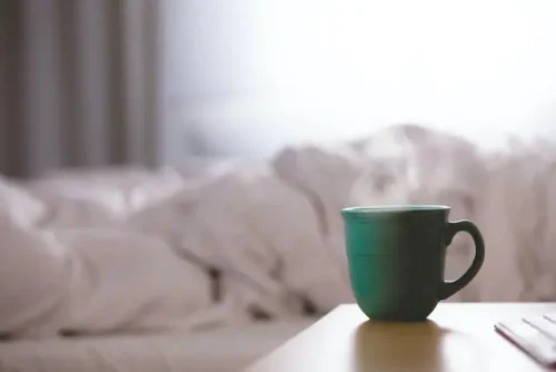 a fresh cup of coffee with an unmade bed in the background