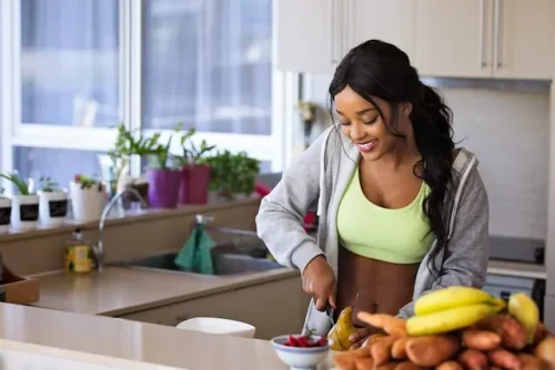 Woman wearing a sports bra and a hoodie preparing food in her kitchen