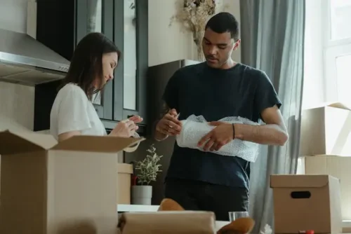 Man and woman using bubble wrap for packing boxes organised during moving process