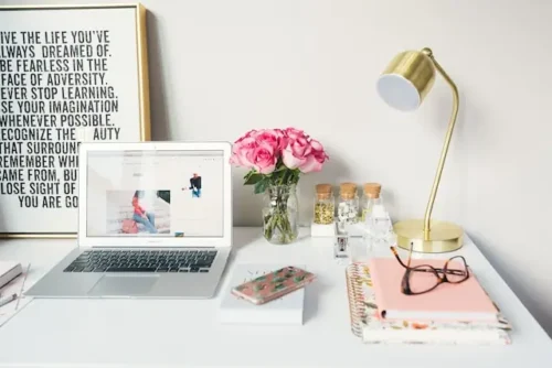 Desk with a laptop, poster, lamp, and flowers on it