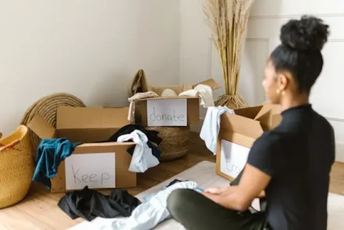 Woman sorting clothes into keep, donate, and trash boxes.