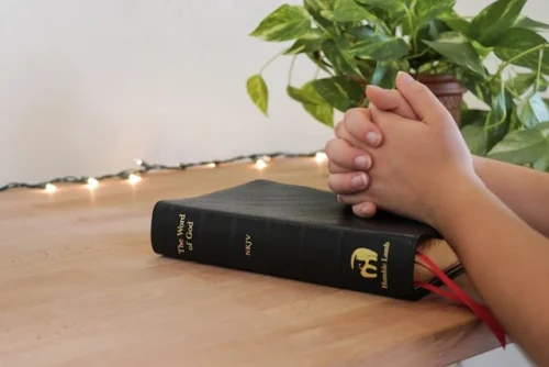 Person praying with an open Bible on a desk, seeking wisdom.