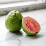 Can diabetics eat guava safely? A whole and halved fresh pink guava on a clean white marble countertop.